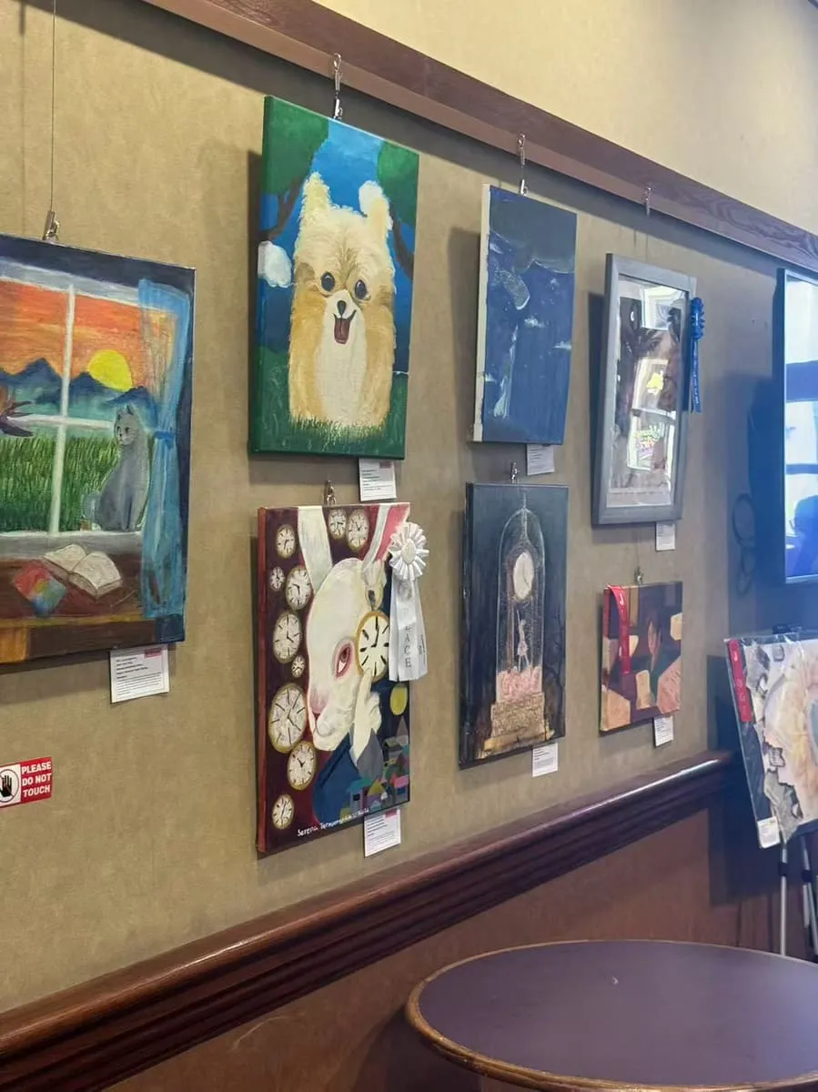 Children’s paintings, from a puppy portrait to a night city, hang in rows on a lobby wall.