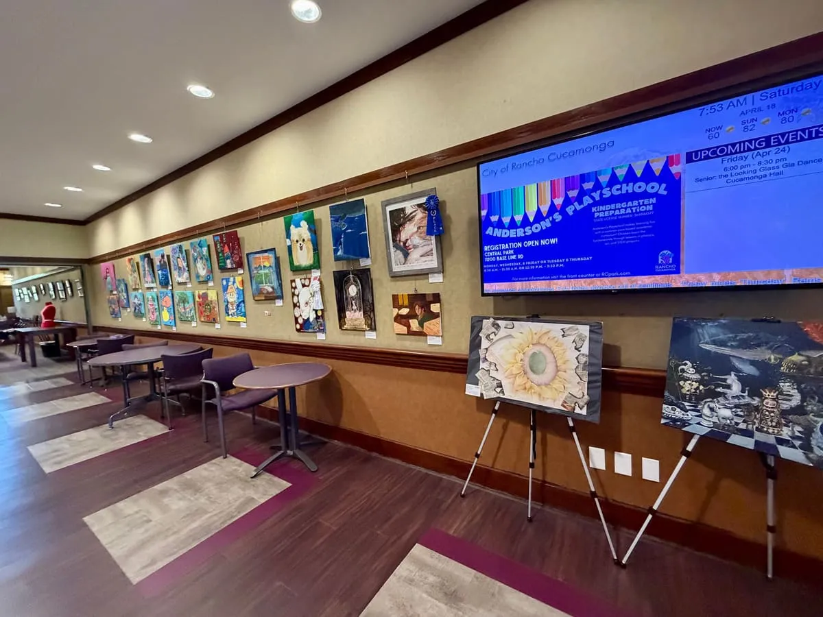 Paintings line the long wall of the community center lobby, with more on easels in front.