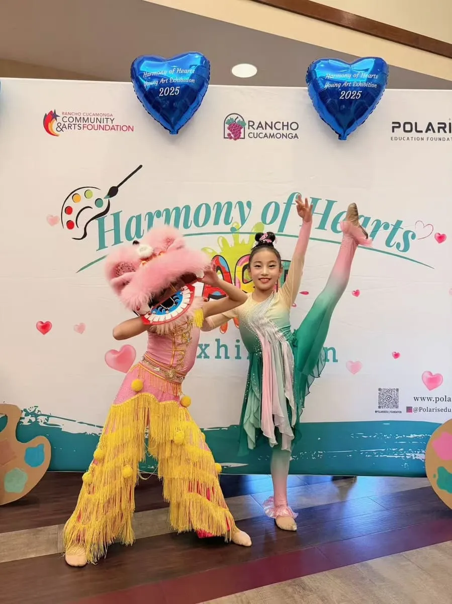 A lion-dance performer and a young dancer pose in front of the backdrop.