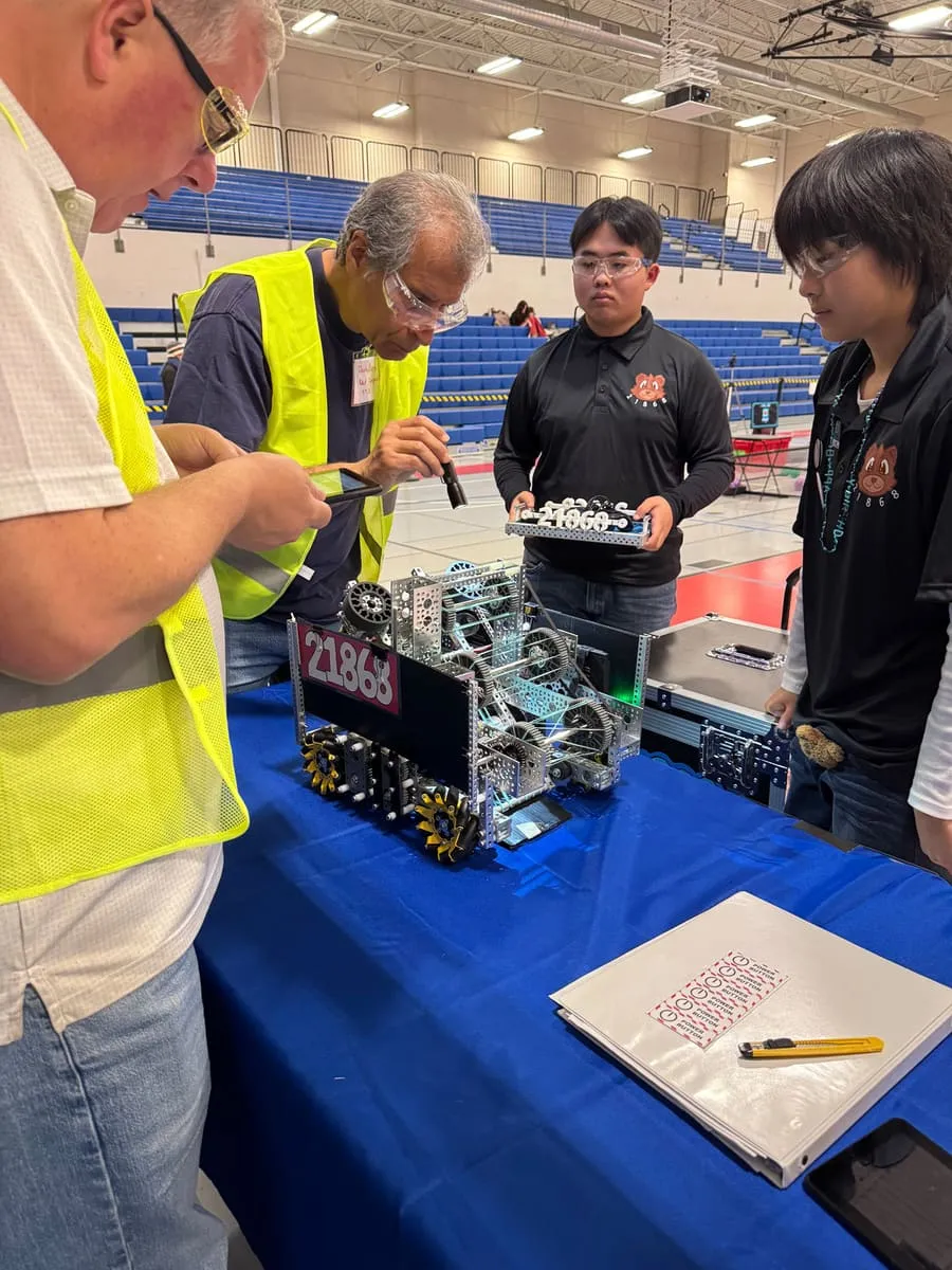 Inspectors in hi-vis vests check a robot at a competition.