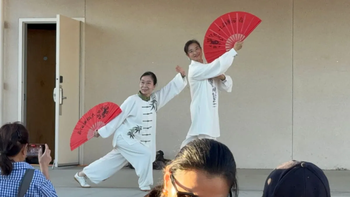 Two performers in white move through a fan routine with red fans.