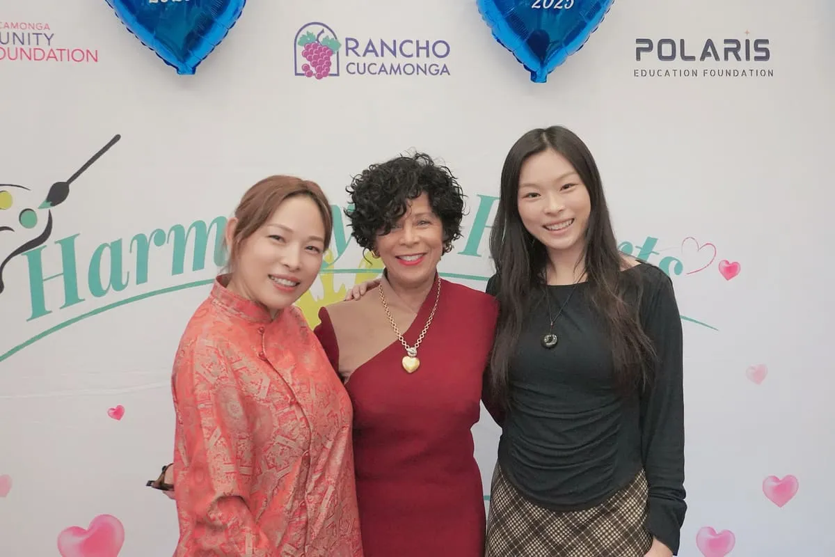 Three women smile in front of the Harmony of Hearts backdrop.