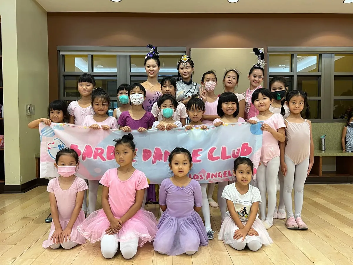 Barbie Dance Club students in pink leotards gather behind their club banner.