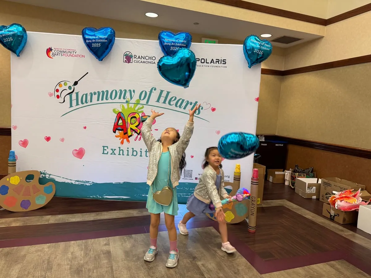 Two girls pose with a heart balloon in front of the Harmony of Hearts backdrop.