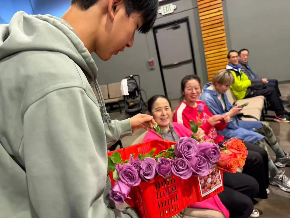 A teenager hands a basket of roses to seniors.