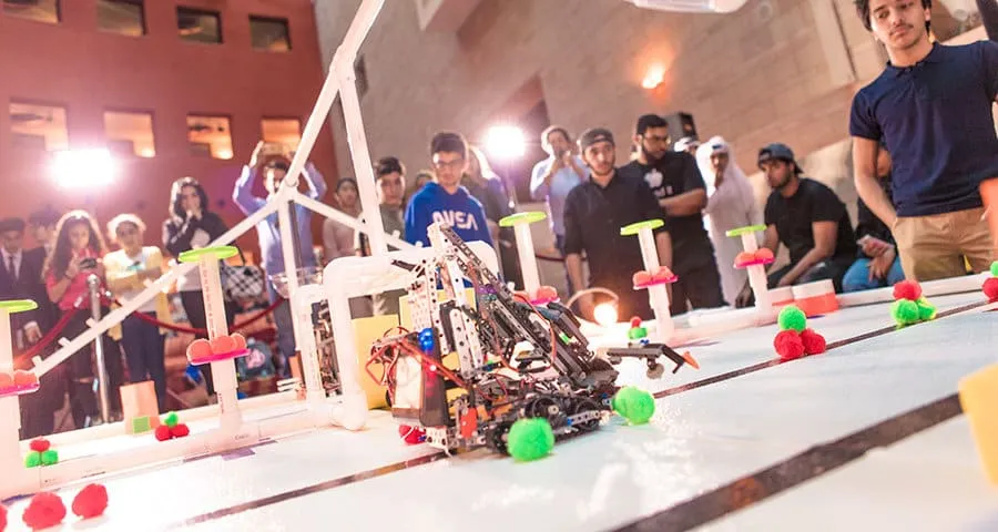 A robot drives across the competition field as students watch.