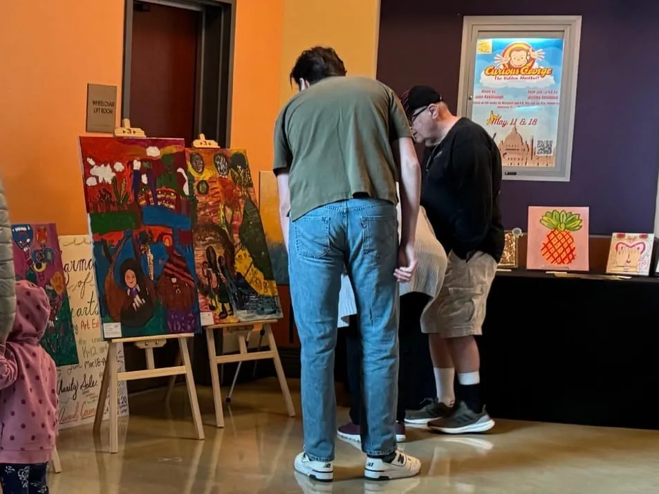 Two visitors study large paintings displayed on easels.