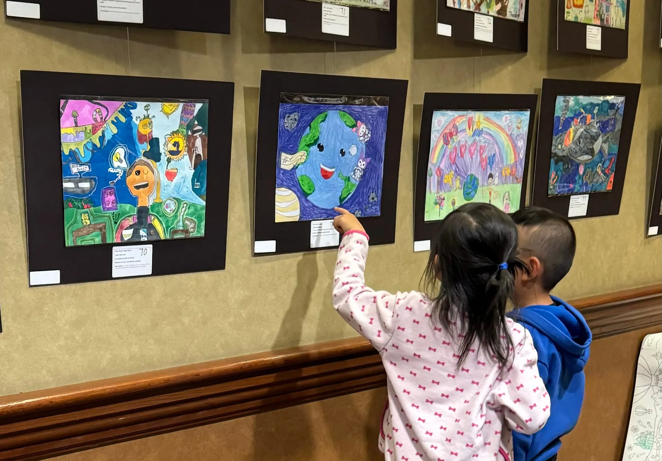 Two young children reach up to point at a painting of the Earth on the exhibition wall.