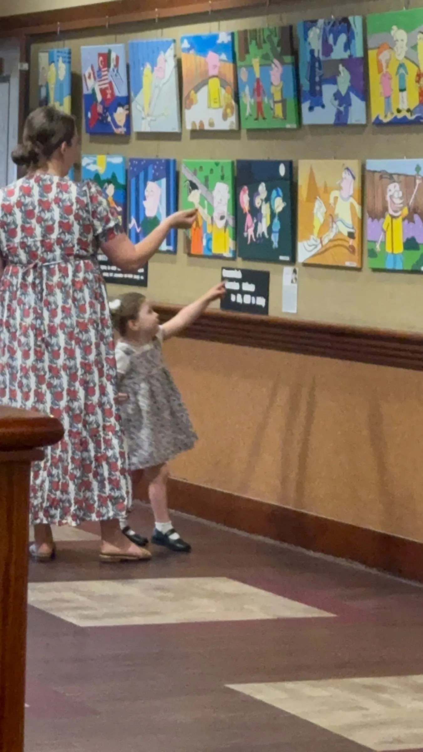 A mother and her toddler point at a row of colorful paintings.