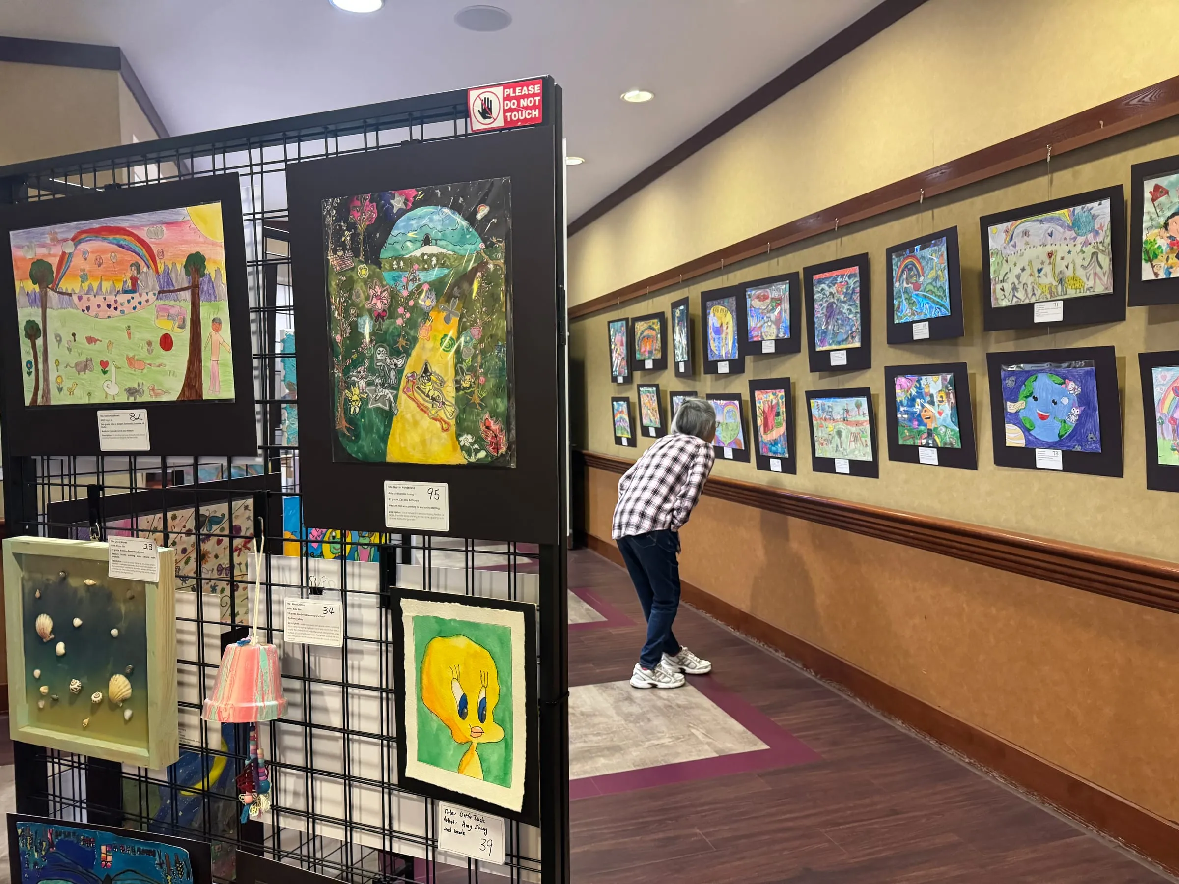 Display panels and a long wall of framed student paintings, with a visitor looking closely at one.
