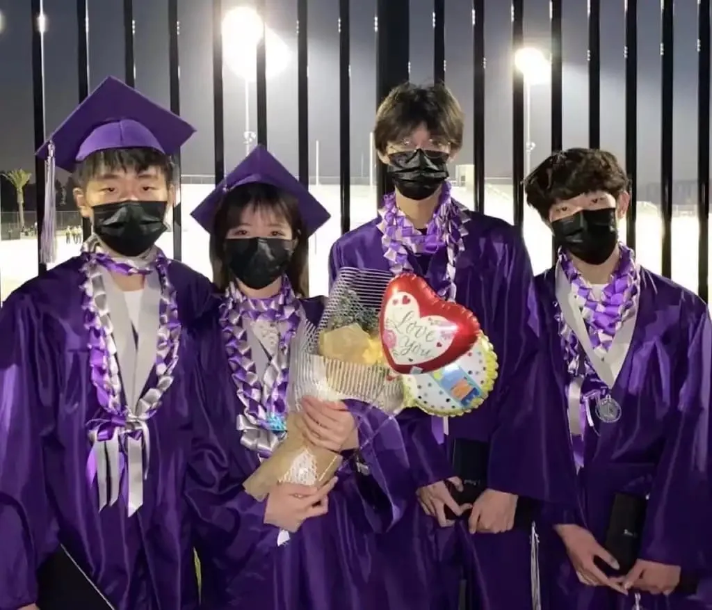 Four graduates in purple caps and gowns wearing purple and silver ribbon leis.